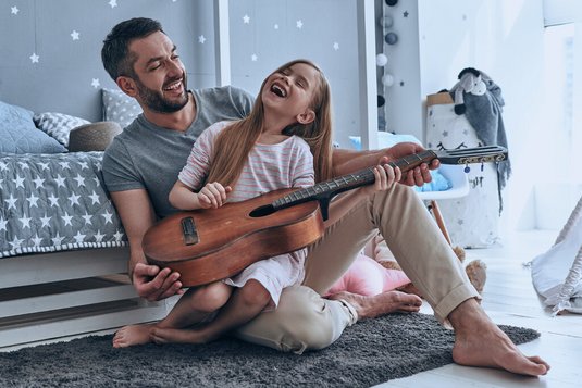 Junger Vater bringt seiner Tochter das Gitarre spielen bei.